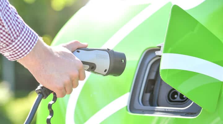 Großaufnahme einer Hand mit Ladekabel vor einem eAuto mit geöffneter Ladeklappe als Symbol für den medl-Geschäftsbereich eMobilität