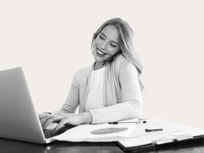 Eine lächelnde Frau telefoniert und arbeitet an einem Laptop, Symbol für den medl-Kundenservice, der online und telefonisch rund um die Uhr erreichbar ist.